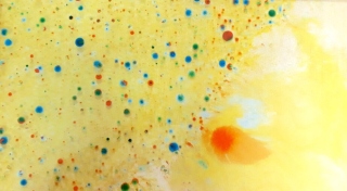A close up photograph of an example of a bath of water coloured yellow with blue and red random sized ink spots.