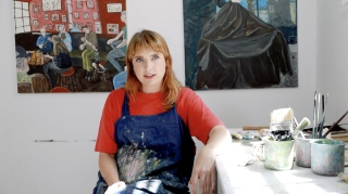 Kathy Tynan sits in her studio wearing a paint-covered apron