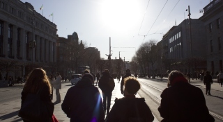 A group of people walk down a Dublin street on a sunny day.