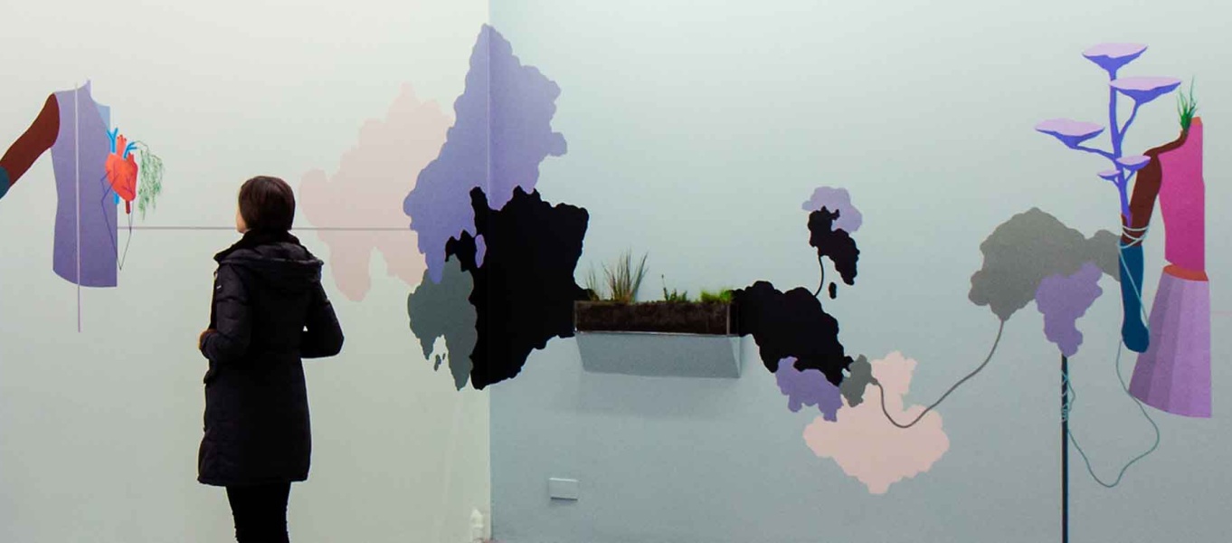 An image of girl by a lake. A hand reaches out from out of frame and places a cowboy hat on her head.