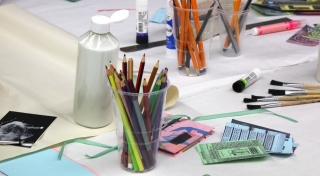 Coloured pencils, glue, and paint brushes are laid out on a table.
