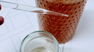 A close up photo of a person holding a pipette in front of jars of liquid