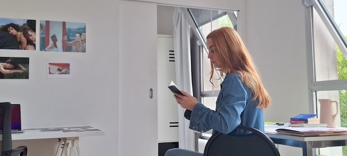 The artist Lisa Freeman sits and reads at her desk in a light-filled studio.