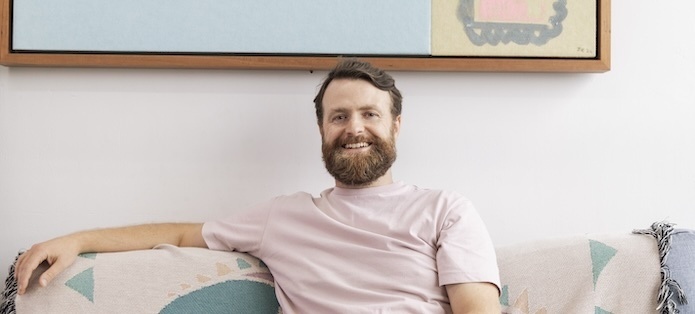 A cropped photo of artist John Conway sitting in his studio smiling